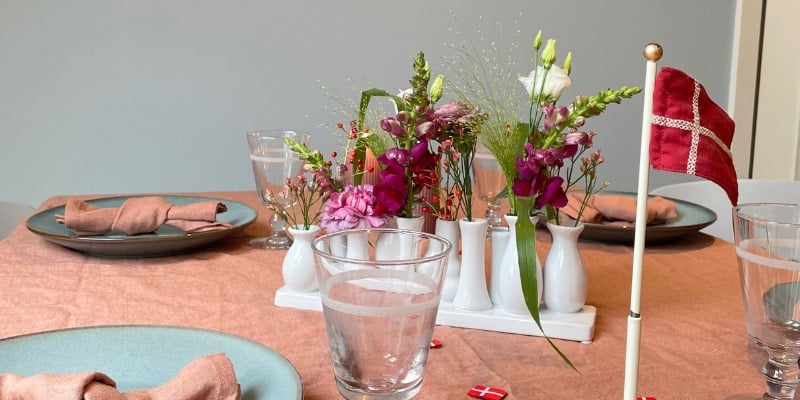 Bord dækket med rosa dug, vase med blomster i forskellige farver.