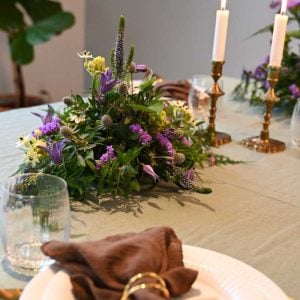 Bordpynt i lilla farver på bord opdækket til middag med tallerken og glas, på grøn dug