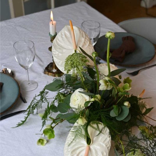 Hvid bordpynt med anthurium og andre blomster på bord