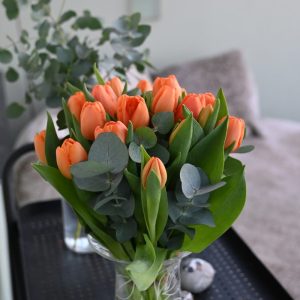 Buket orange tulipaner i en gennemsigtig glasvase, der står på et sort rullebord i hjemlige omgivelser.