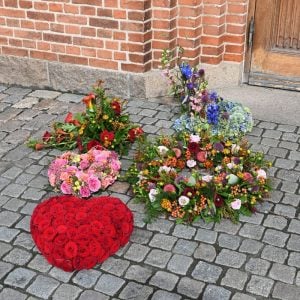 En begravelseskrans med opsats, rødt blomsterhjerte, begravelseskrans, åbent blomsterhjerte og begravelsesdekoration udenfor kirke