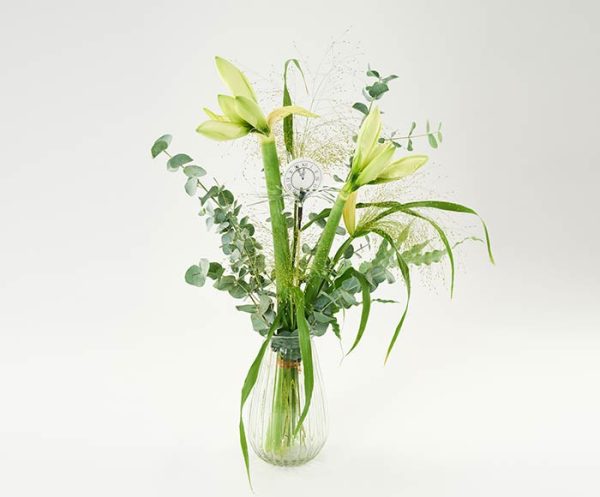 En buket af hvide amaryllis, eucalyptus, græsser og nytårspynt, står i en gennemsigtig vase.