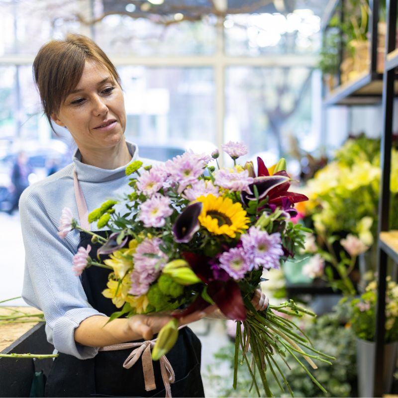 Blomsterdekoratør står i sin blomsterbutik og binder en stor, flot, multicolor buket.